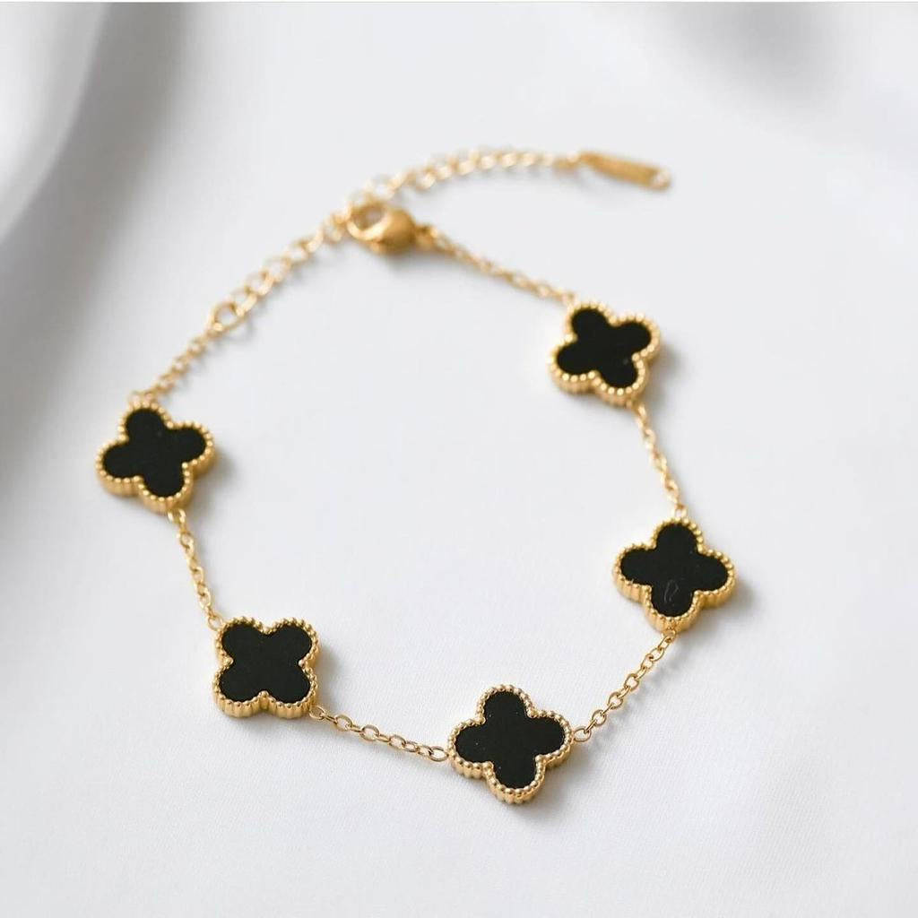 Gold bracelet with black clover-shaped charms on a light gray background