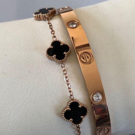 A rose gold bracelet displayed on a white textured surface, featuring a Cartier-style link bracelet alongside a matching rose gold chain bracelet with black enamel four-leaf clover charms.