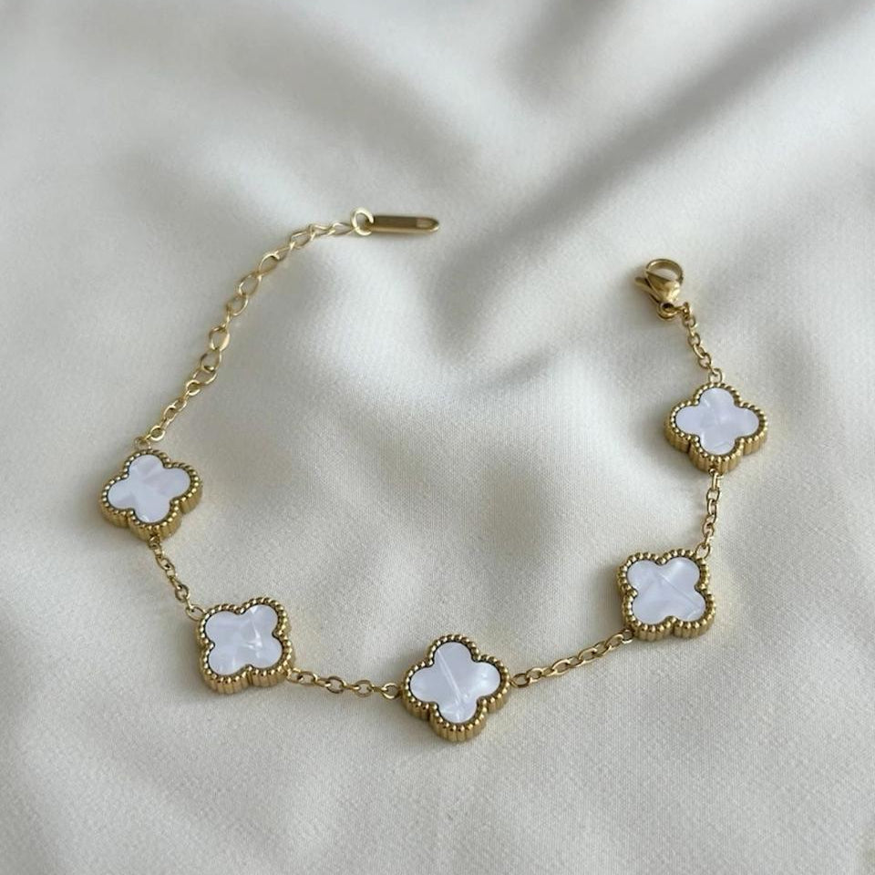 Gold bracelet with white clover-shaped charms on a beige fabric background